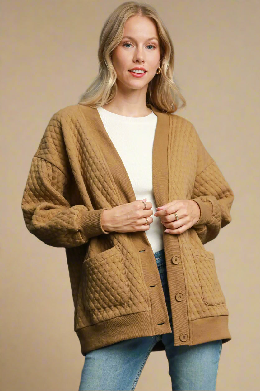 Woman wearing a brown quilted cardigan over a white shirt and blue jeans on a beige background