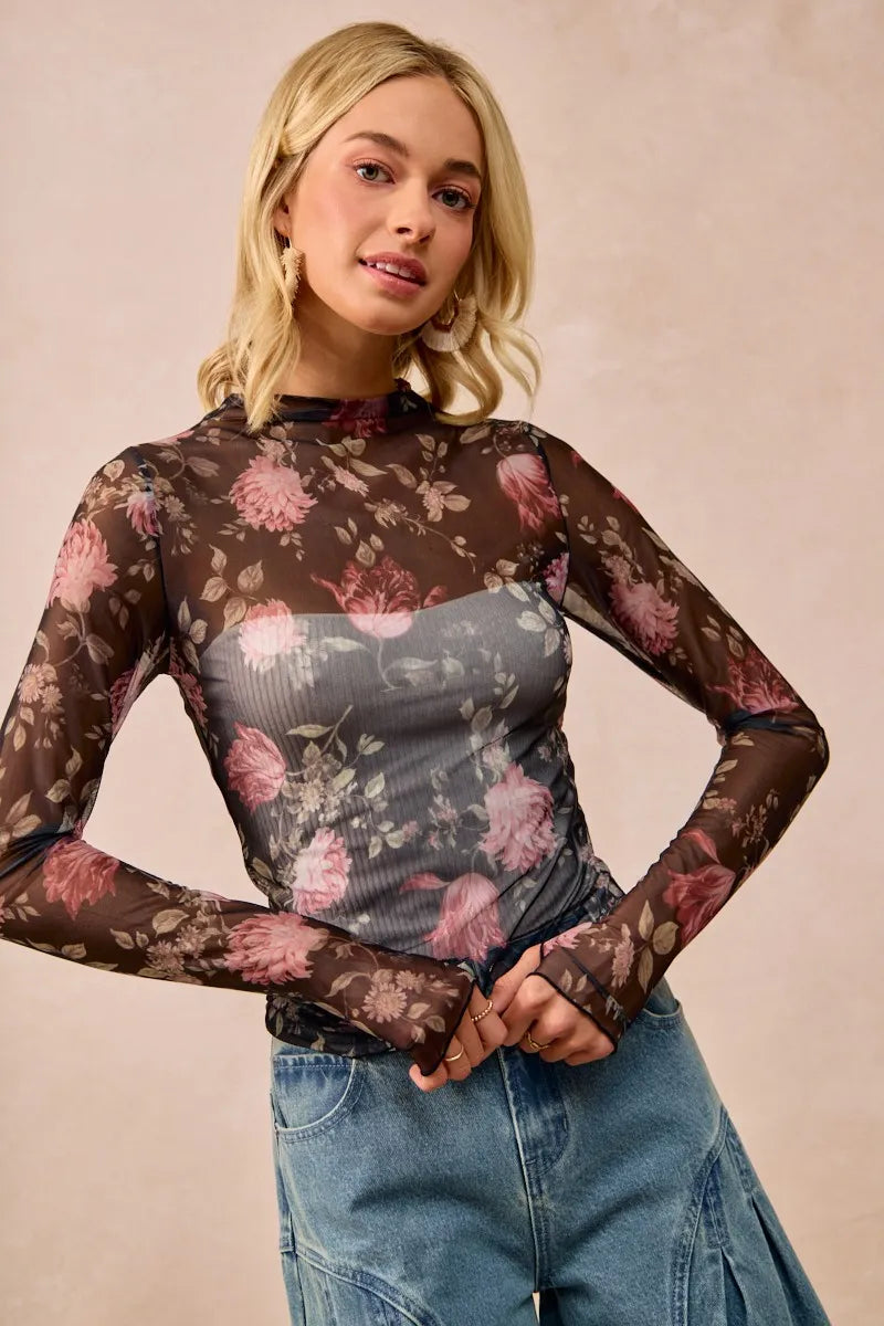 Woman wearing a floral sheer long-sleeve top and jeans against a beige background