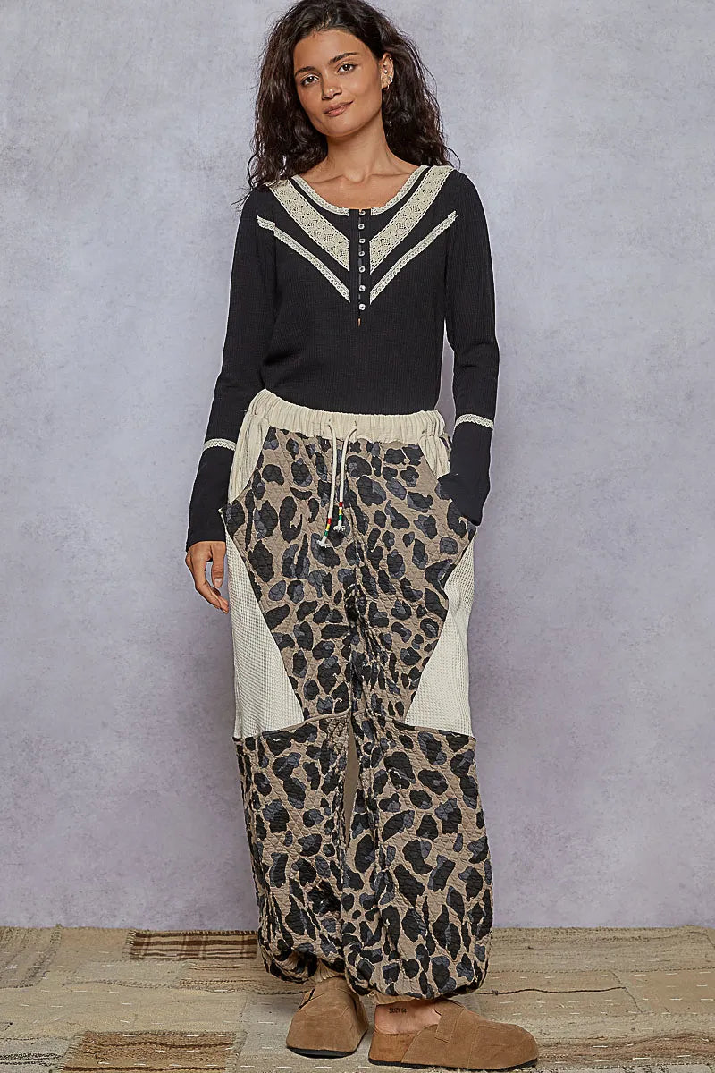 Woman wearing a black long-sleeve top and leopard print pants against a gray background