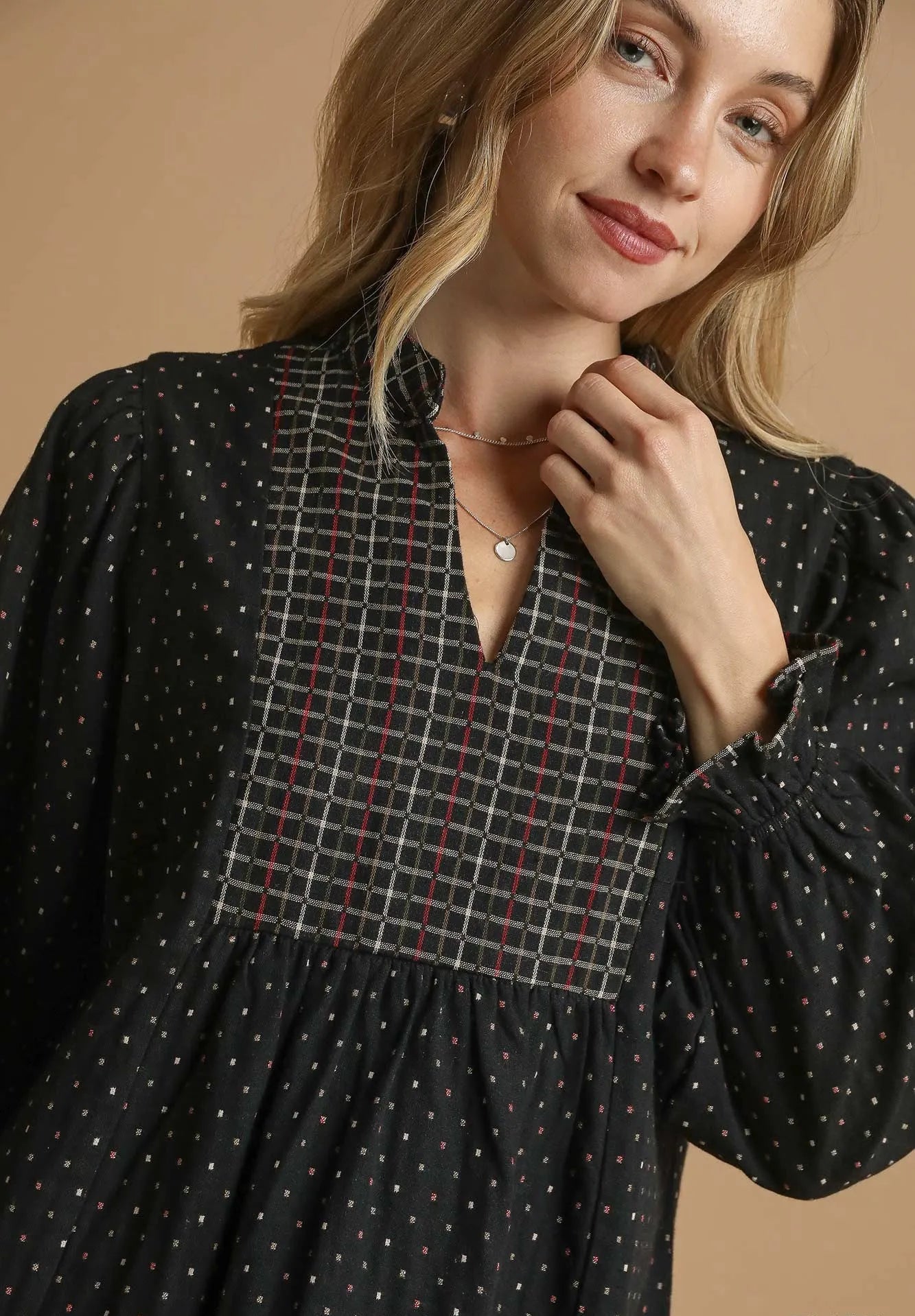 Woman wearing a black dress with a patterned neckline against a beige background