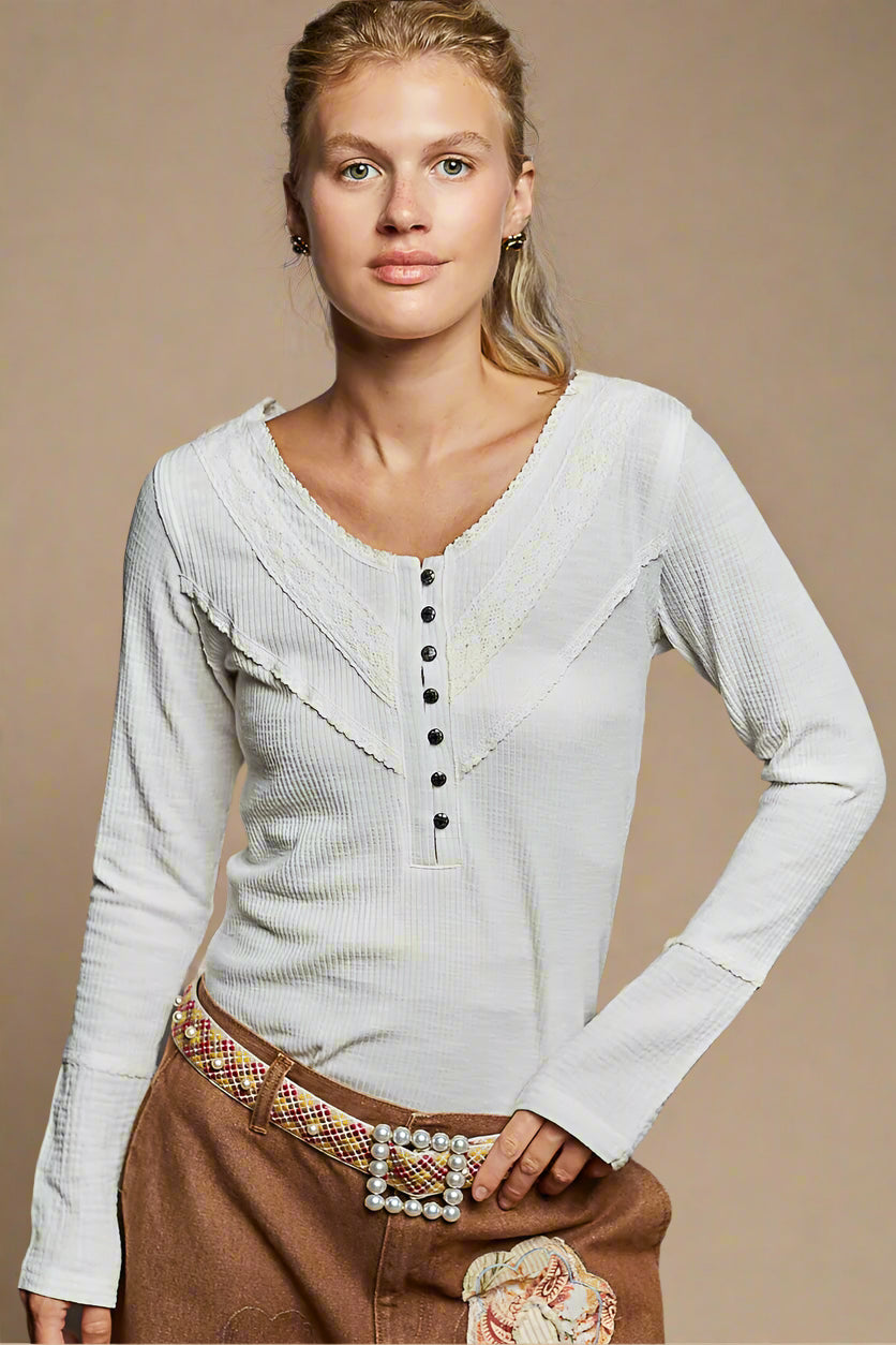 Woman wearing a light gray long-sleeve top with buttons and brown pants against a beige background