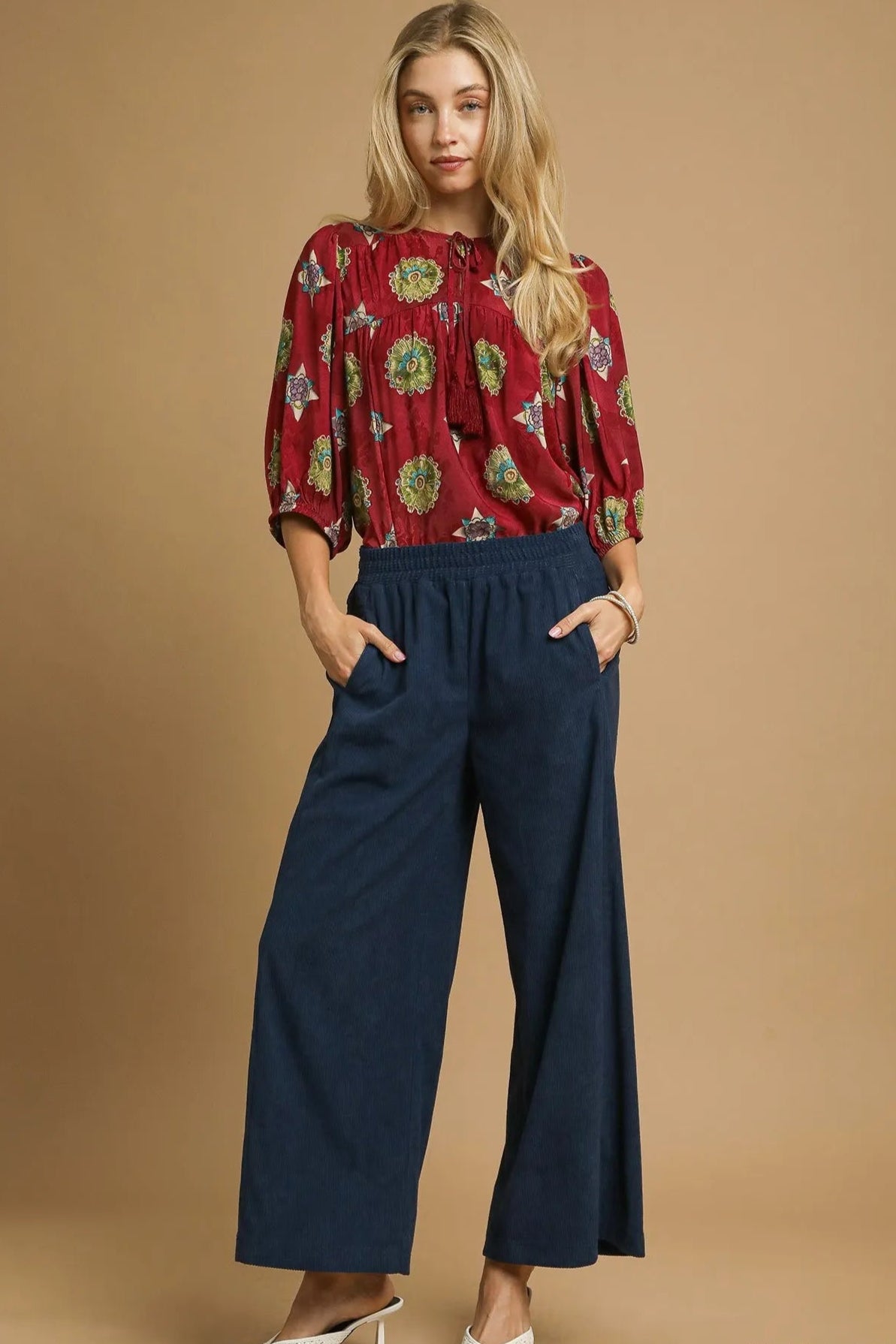 Woman wearing a red floral blouse and navy blue pants on a beige background