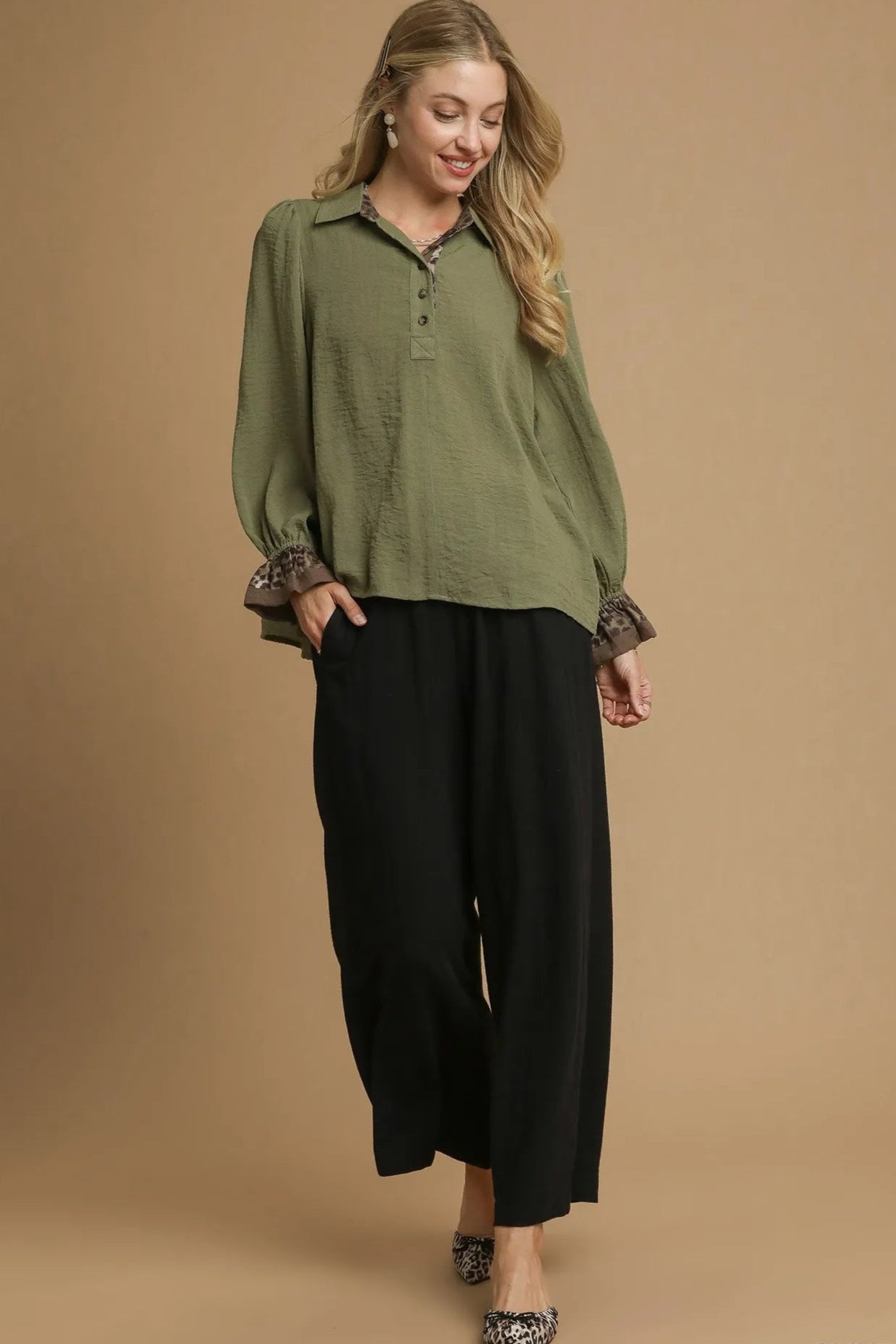 Woman wearing an olive green top and black pants on a beige background