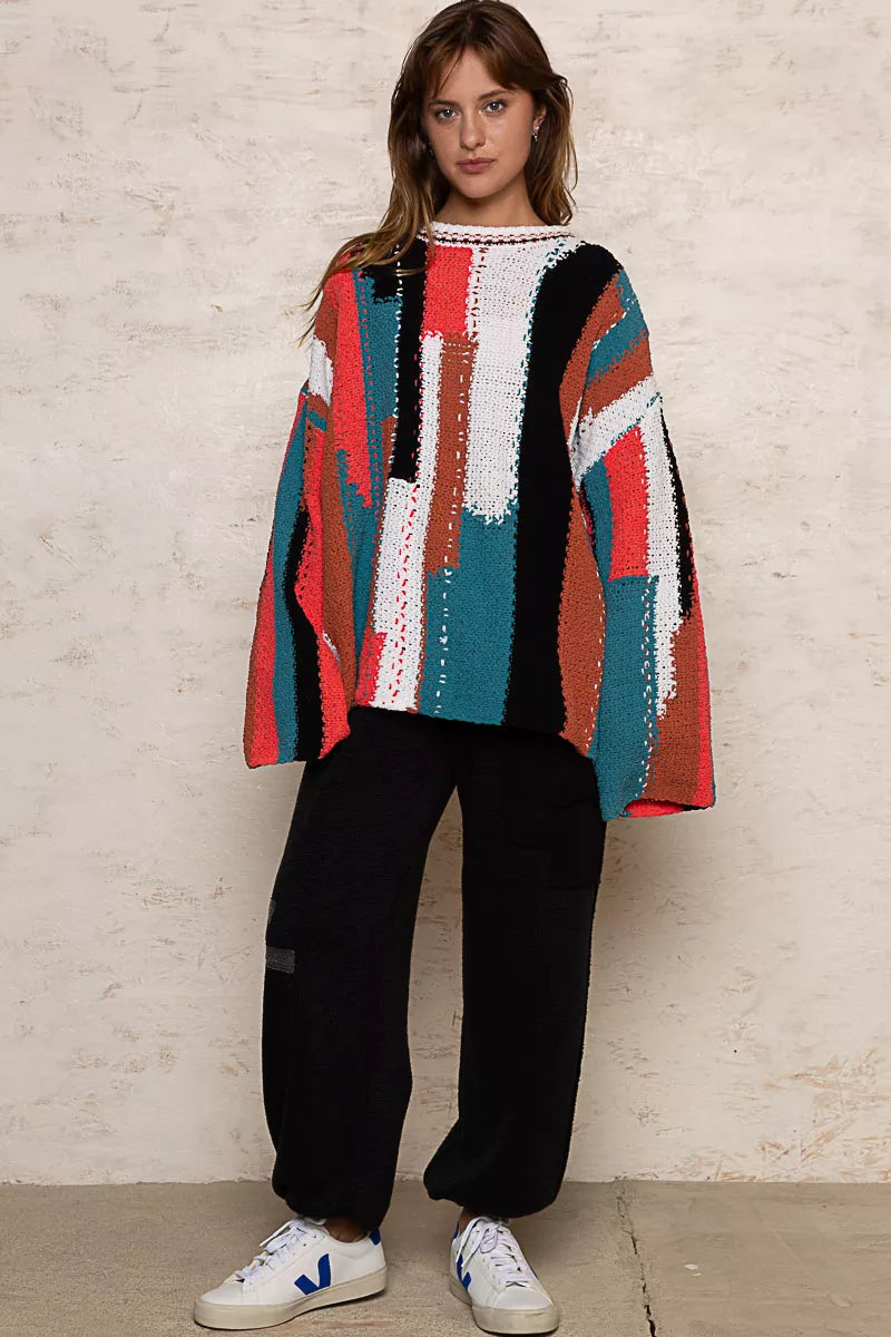 Person wearing a colorful striped sweater against a white brick wall.