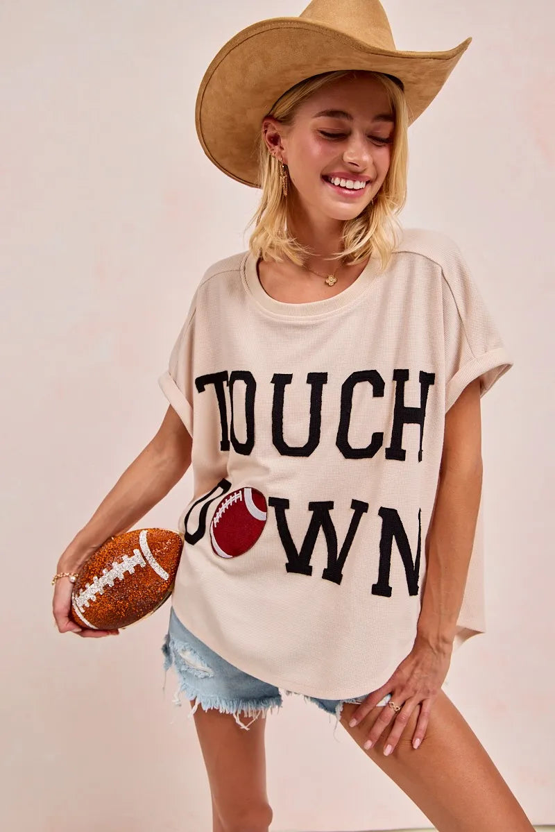 Woman wearing a 'Touchdown' t-shirt and holding a football, smiling.
