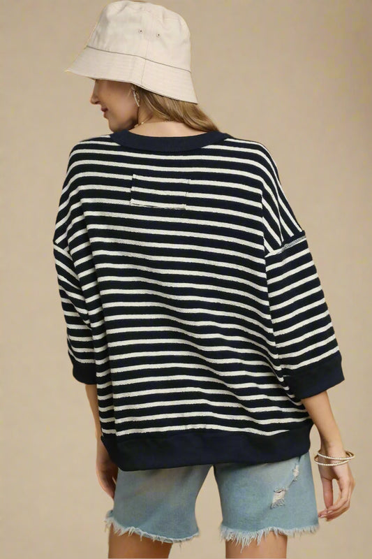 Person wearing a navy and white striped sweater with denim shorts on a brown background