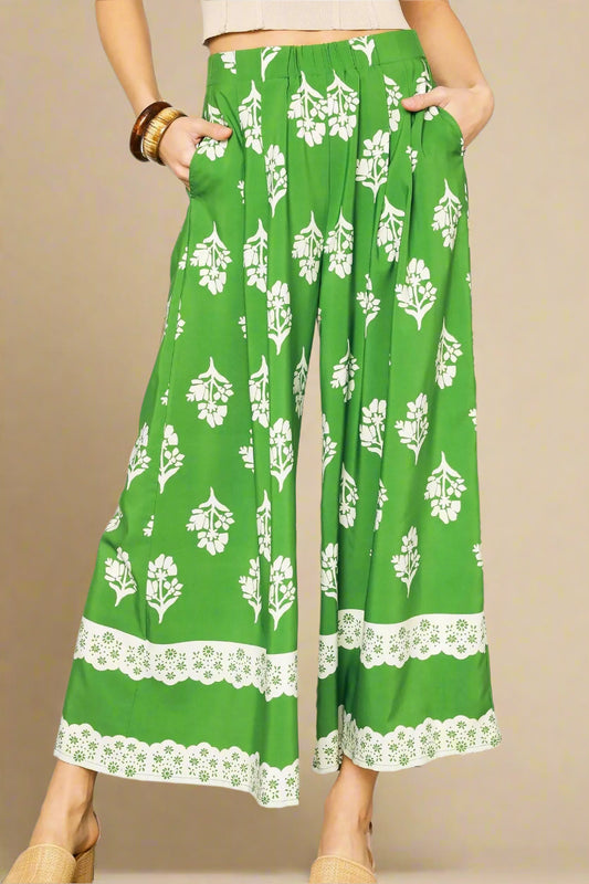 Green pants with white floral pattern worn by a person on a plain background