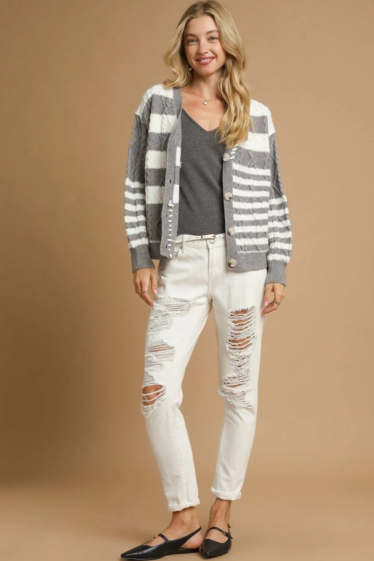 Woman wearing a striped cardigan, black top, and white distressed jeans on a beige background