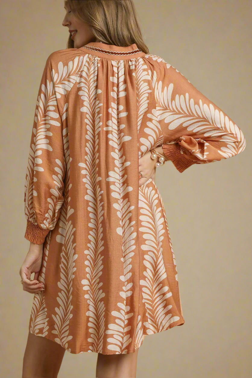 Woman wearing a taupe dress with white leaf pattern on a beige background