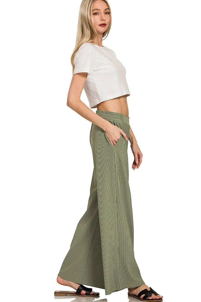 Woman wearing a white crop top and green wide-leg pants on a white background