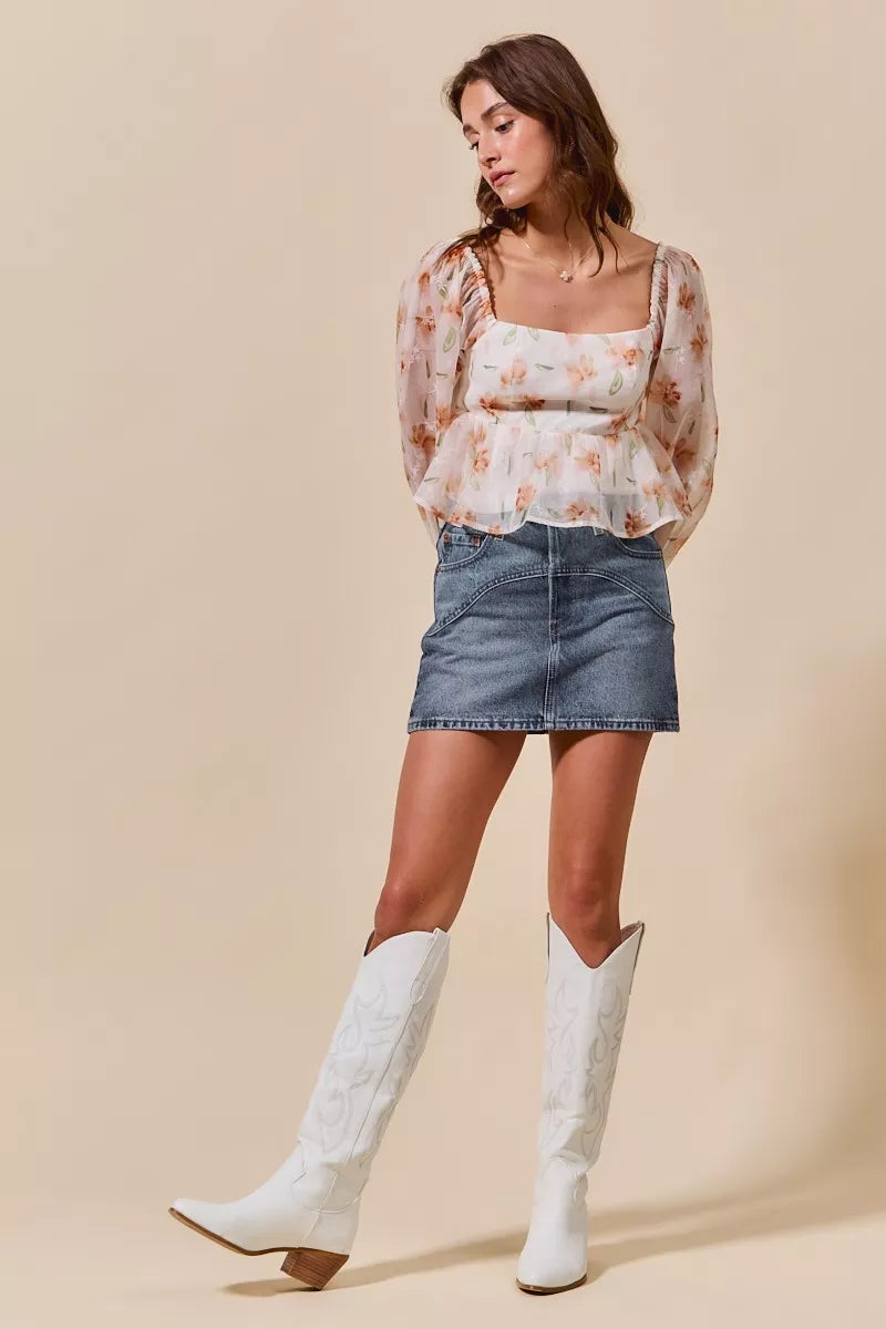 Woman wearing a floral top, denim skirt, and white knee-high boots on a beige background