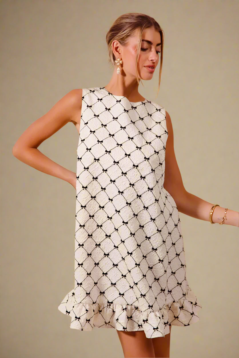 Woman wearing a white dress with black geometric pattern on a beige background
