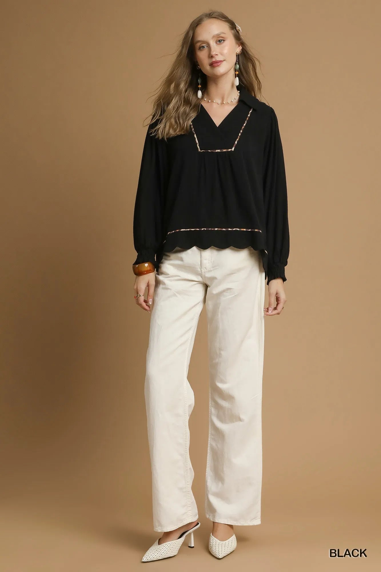 Woman wearing a black blouse and white pants against a brown background