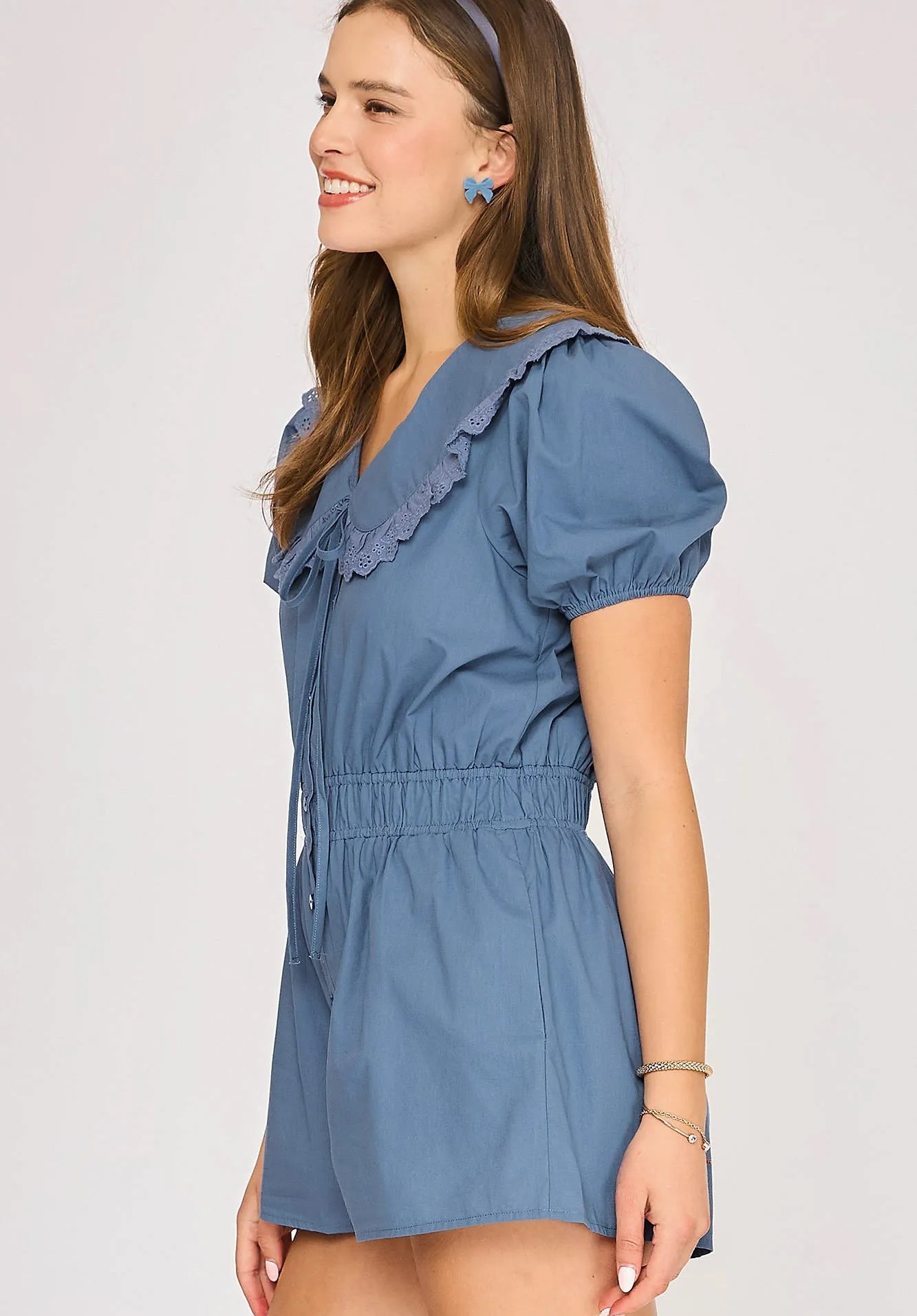 Woman wearing a blue romper with ruffled details on a light gray background