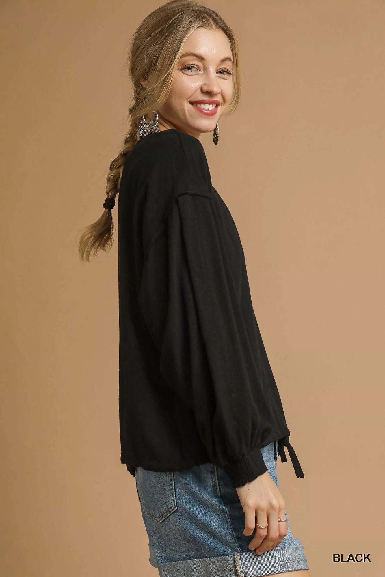 Woman wearing a black top with long sleeves against a brown background