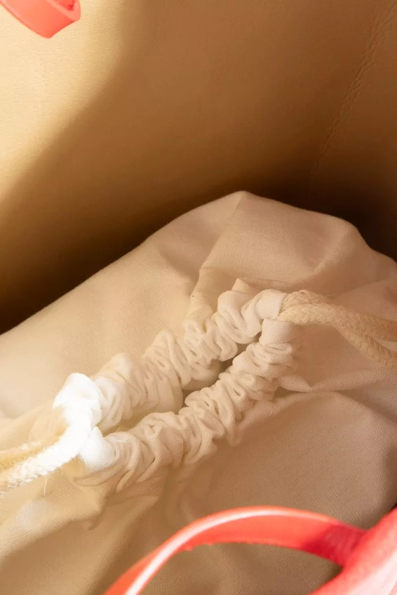 Close-up of a drawstring on a beige bag with a red handle.