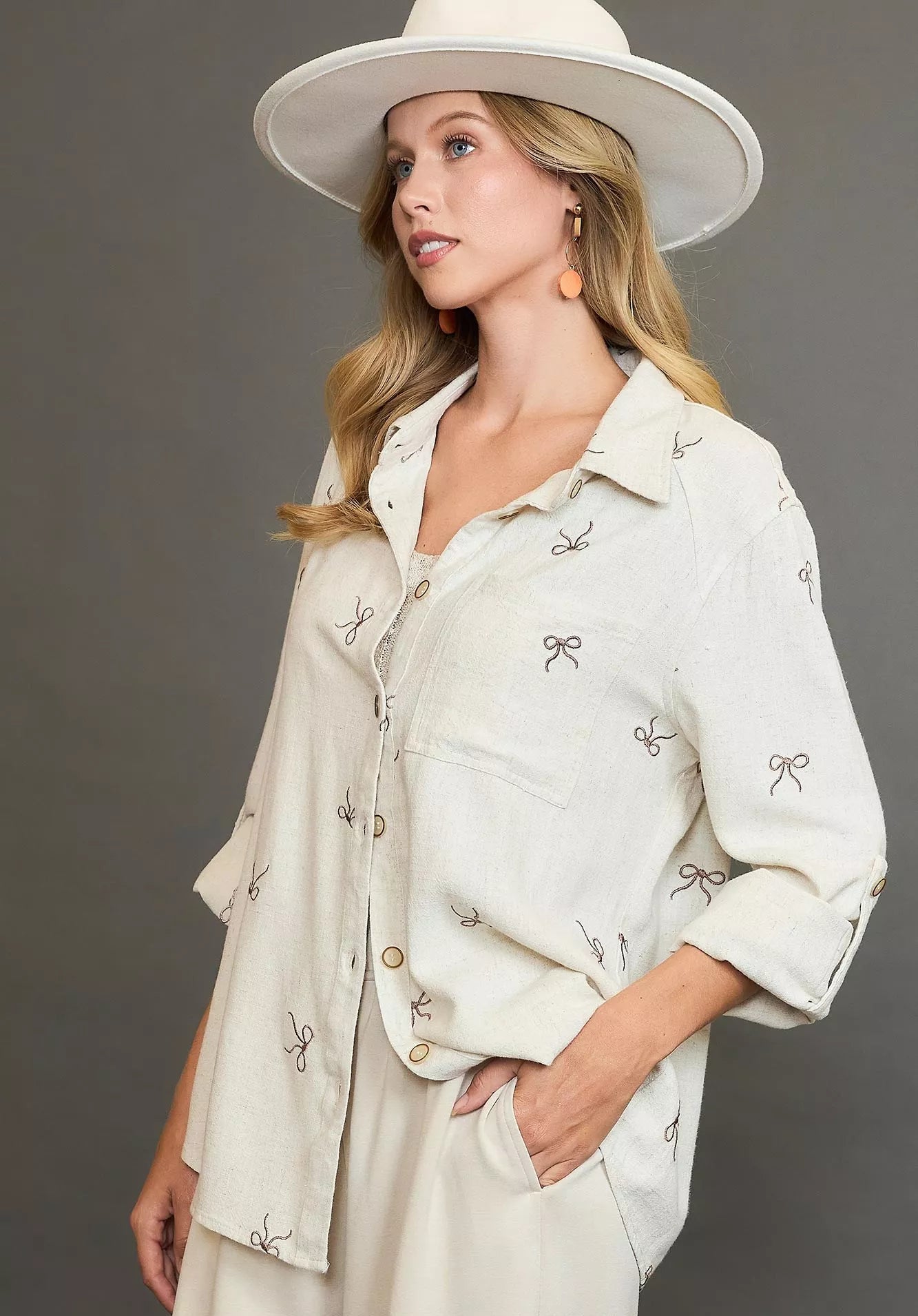 Woman wearing a light-colored outfit with a hat against a gray background