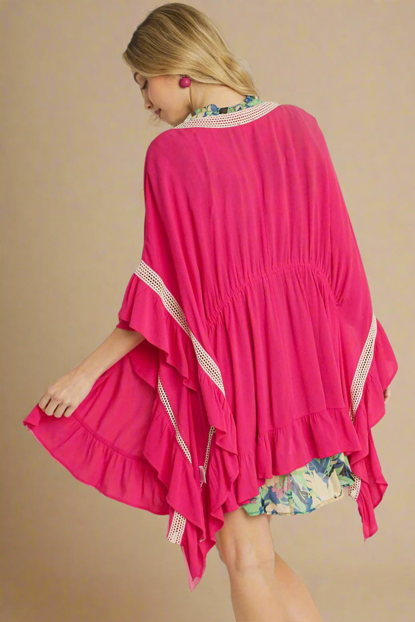 Woman wearing a bright pink cover-up with floral trim on a plain background