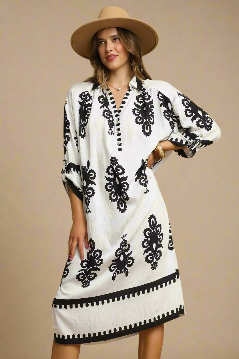 Woman wearing a cream dress with black patterns and a beige hat on a beige background