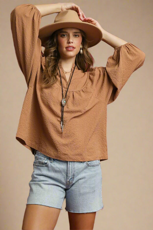 Woman wearing a brown blouse, beige hat, and denim shorts against a beige background
