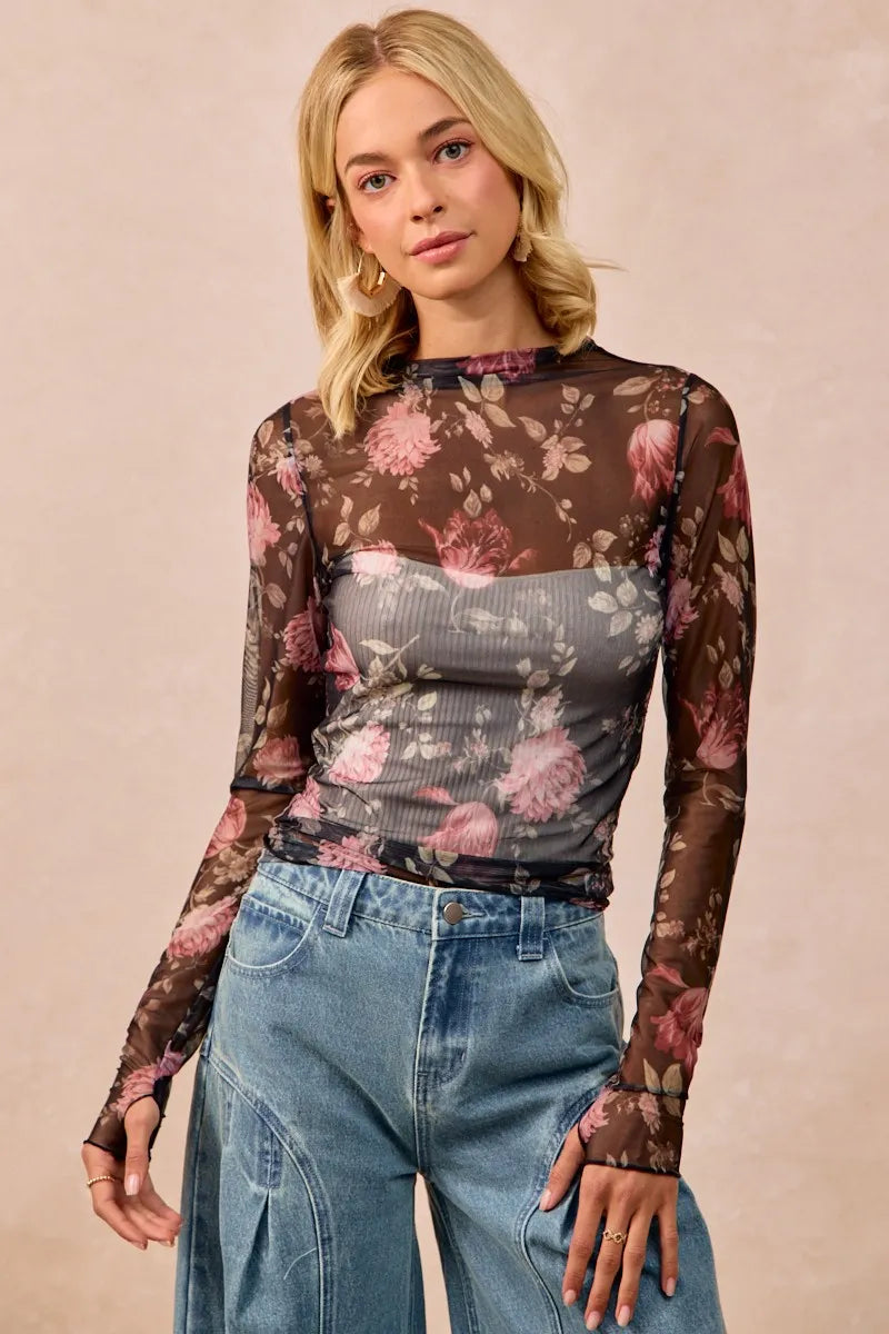 Woman wearing a floral mesh top and jeans against a beige background
