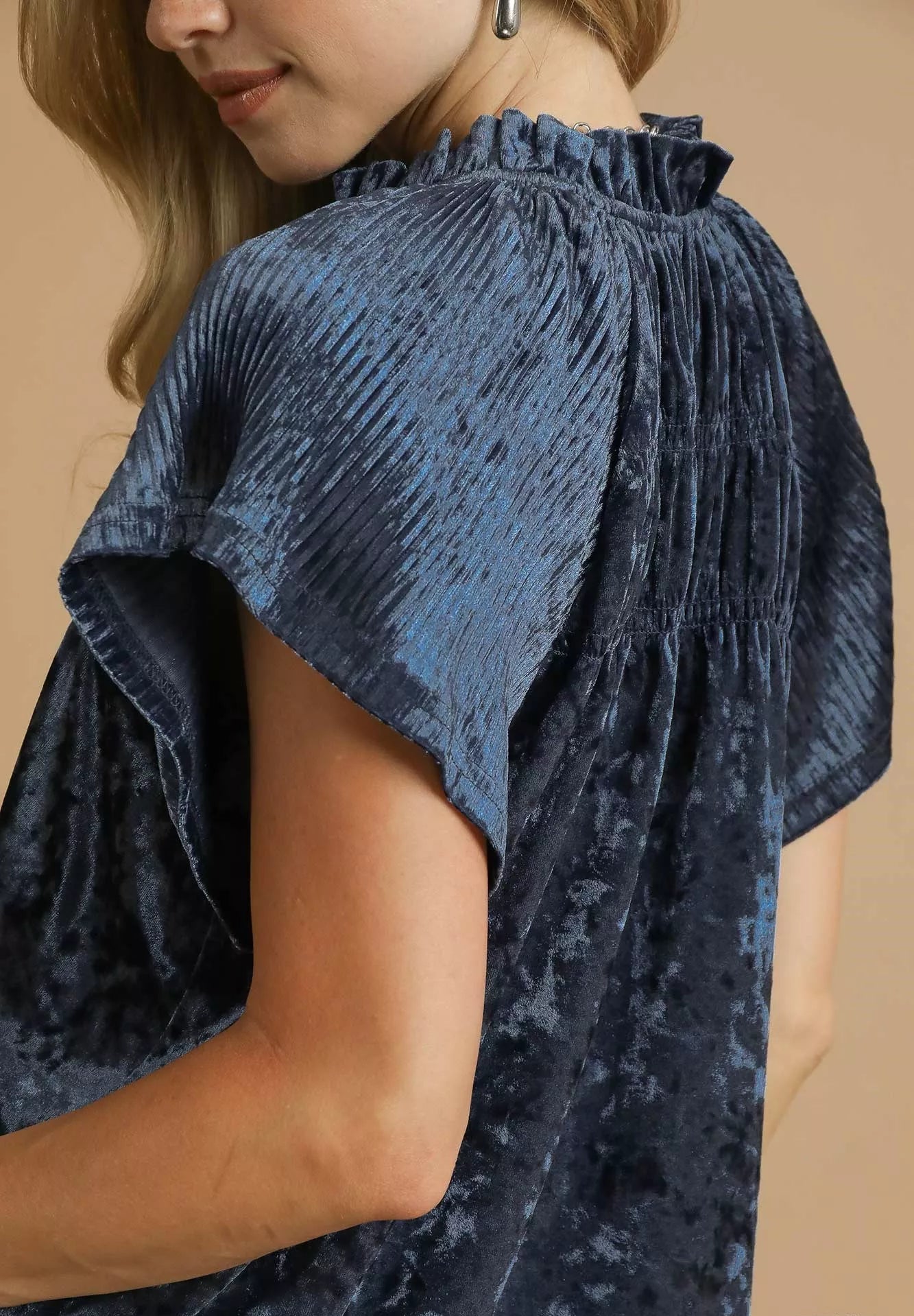 Blue textured blouse with ruffled shoulders on a beige background