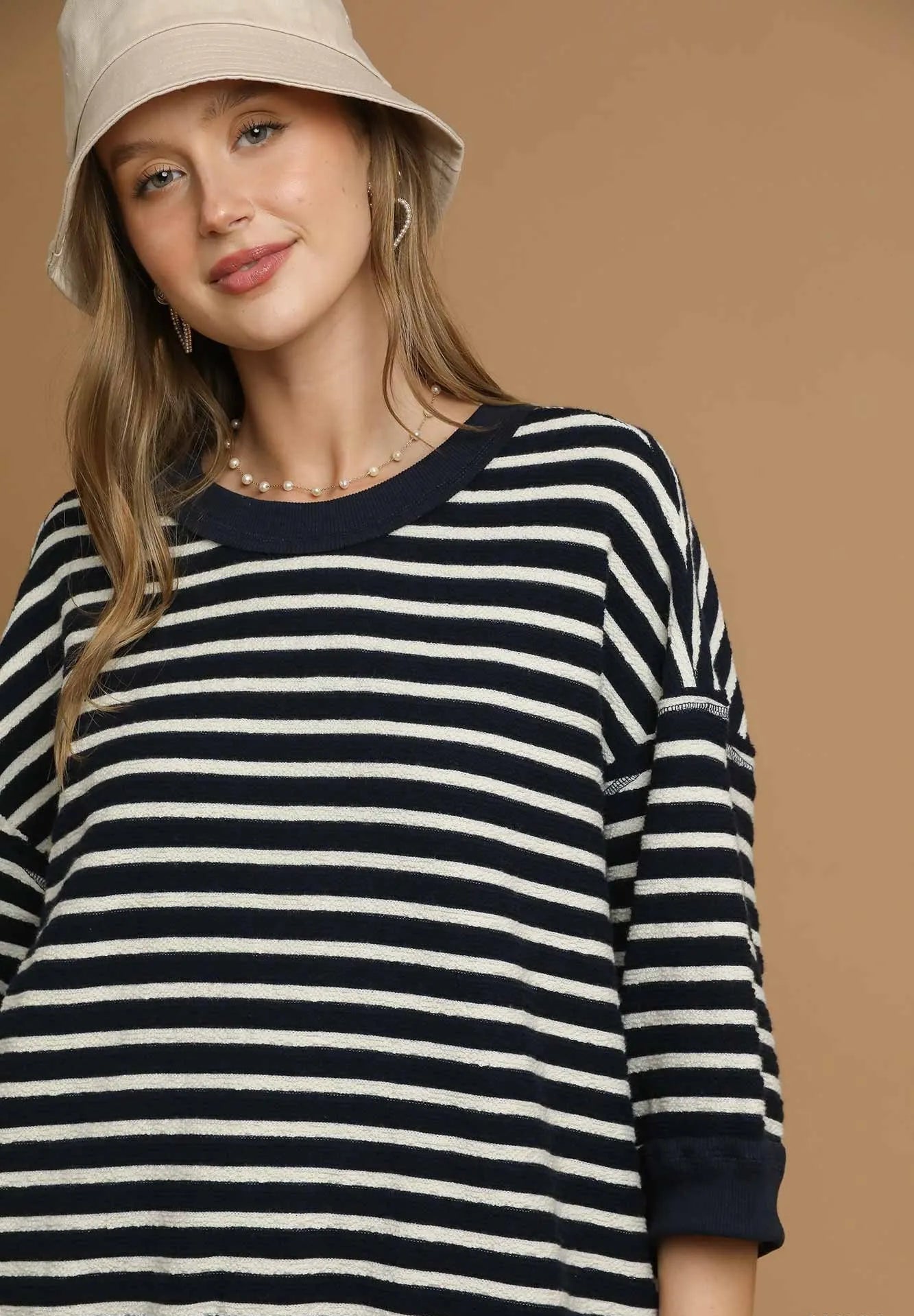 Woman wearing a navy and white striped sweater with a beige hat on a brown background