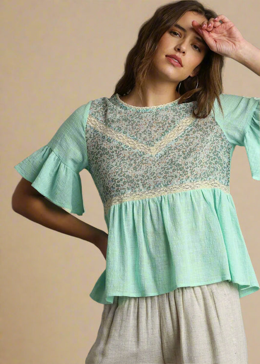 Woman wearing a light green blouse with ruffled sleeves against a beige background