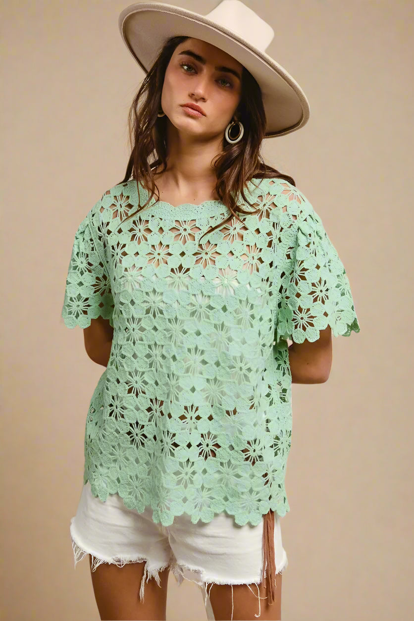 Woman wearing a light green lace top and white shorts with a beige hat on a beige background