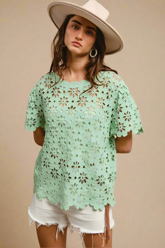 Woman wearing a light green lace top and white shorts with a beige hat on a beige background