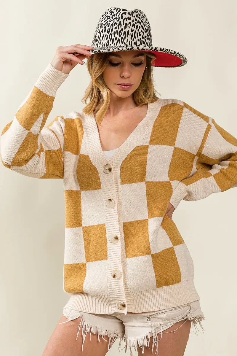 Woman wearing a checkered cardigan and leopard print hat against a plain background