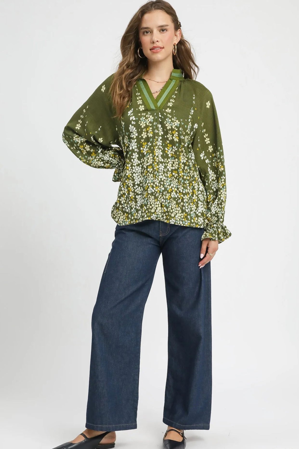 Woman wearing a green floral blouse and blue jeans on a white background