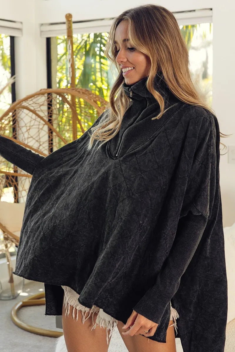 Woman wearing a dark gray oversized sweater in a bright room with plants.