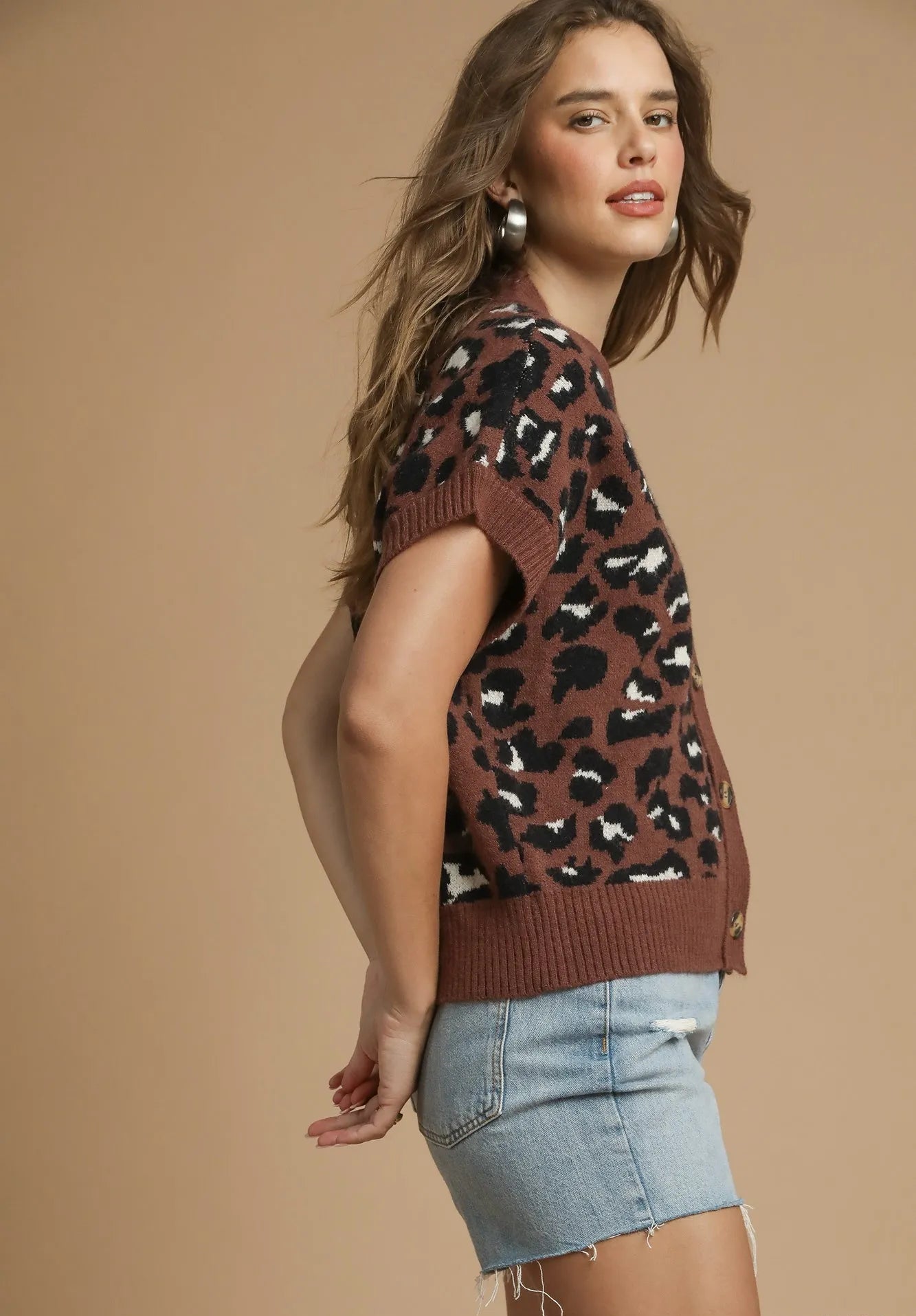 Woman wearing a brown patterned sweater and denim shorts on a beige background