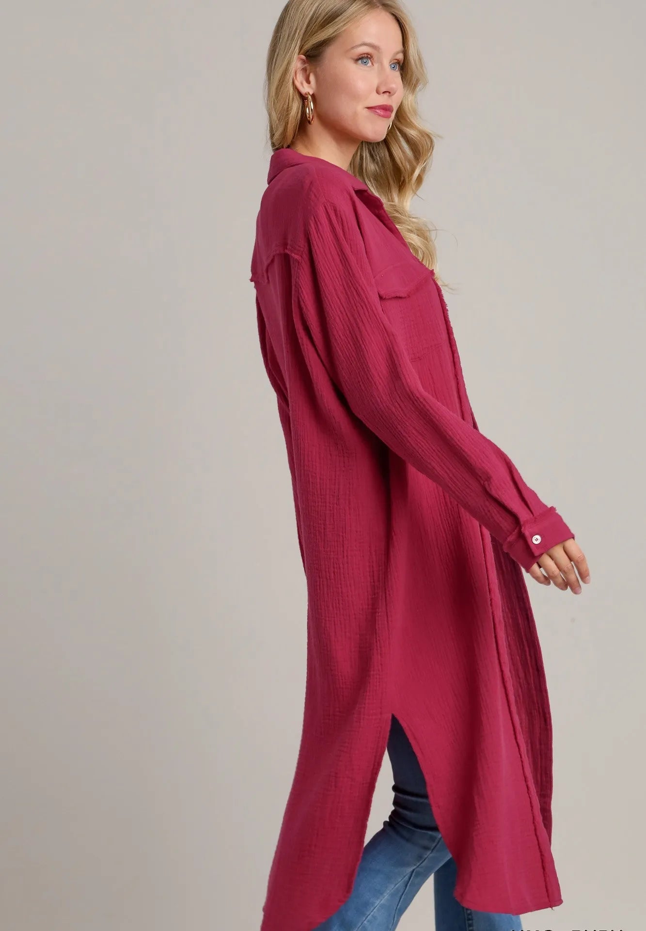 Woman wearing a long burgundy shirt with blue jeans on a plain background