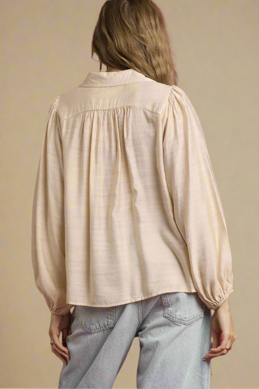 Person wearing a beige blouse and light blue jeans against a red background