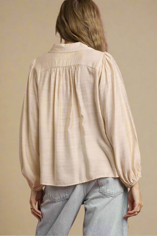 Person wearing a beige blouse and light blue jeans against a red background