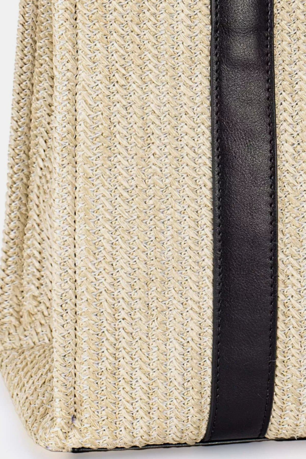 Close-up of a straw bag with a black strap on a light background