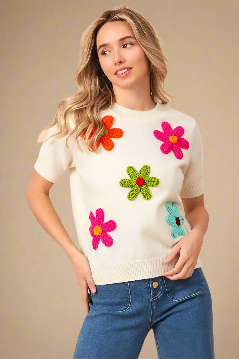 Woman wearing a cream sweater with colorful flower patterns on a beige background