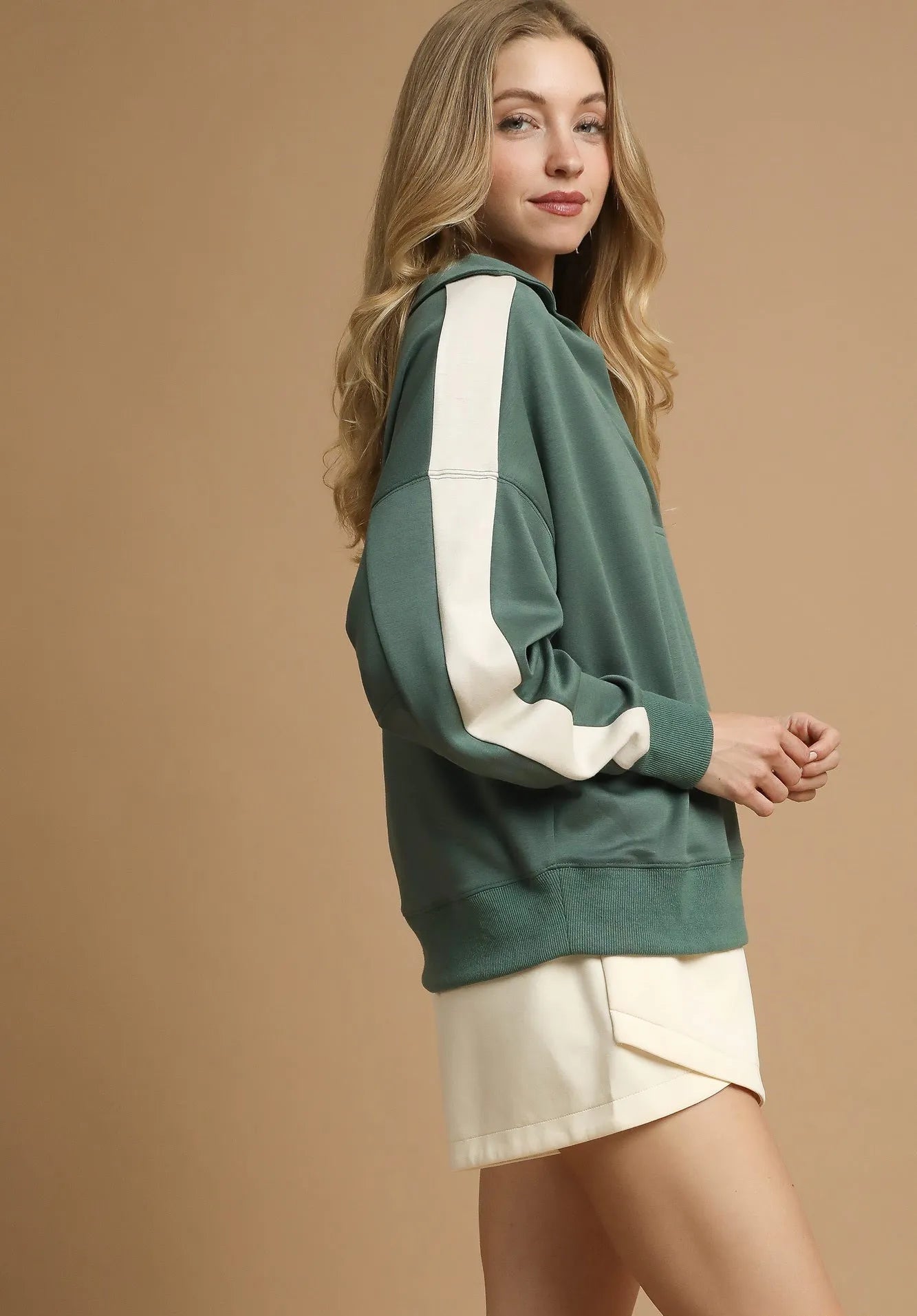 Woman wearing a green and white sweatshirt with a beige background