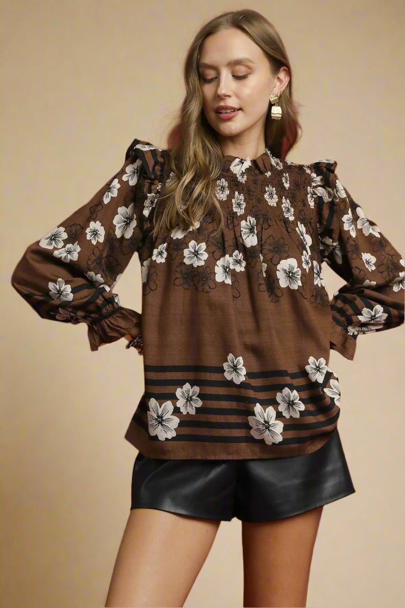 Woman wearing a brown floral blouse with black shorts against a beige background
