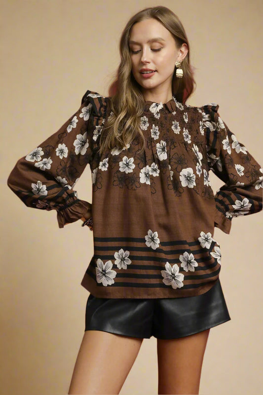 Woman wearing a brown floral blouse with black shorts against a beige background