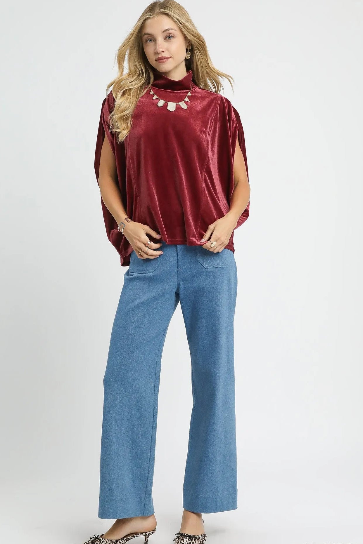 Woman wearing a red velvet top and blue pants on a white background