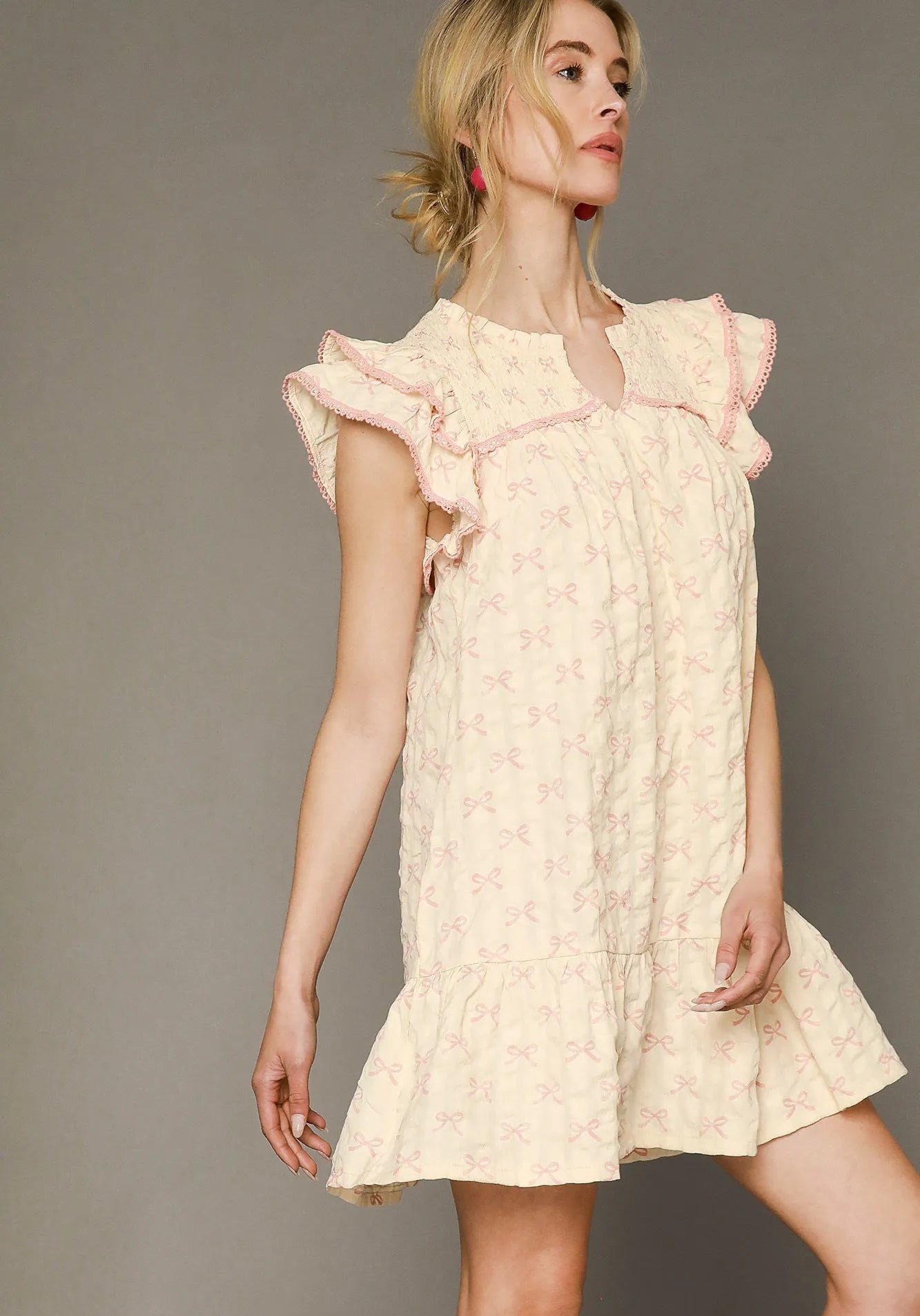 Woman wearing a light pink dress with ruffled sleeves against a gray background