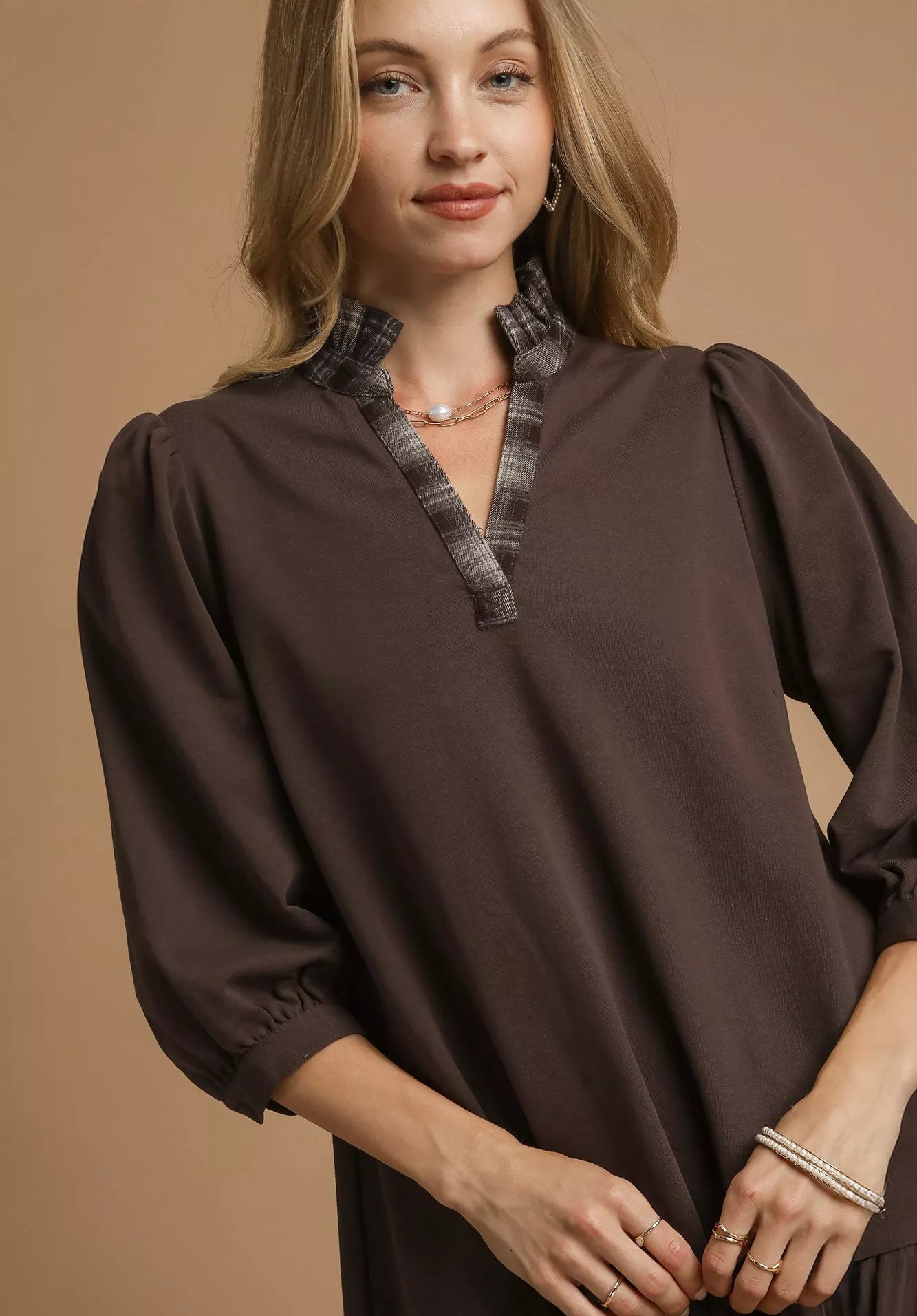 Woman wearing a brown blouse with plaid trim on a beige background