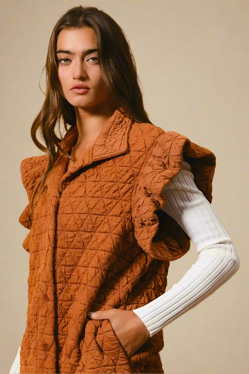 Woman wearing a textured orange vest over a white long-sleeve shirt against a beige background