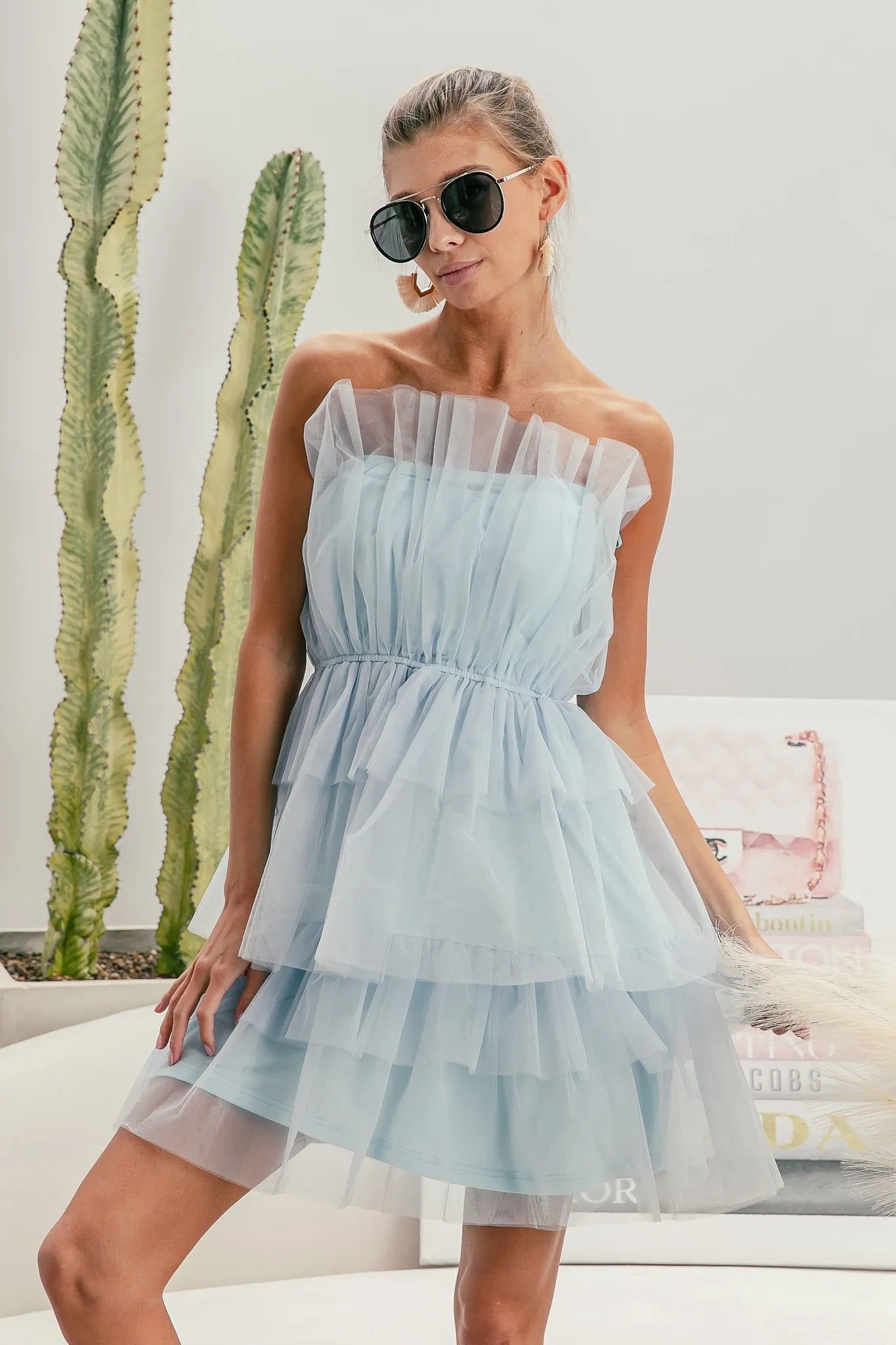 Woman wearing a light blue strapless dress with sunglasses indoors.