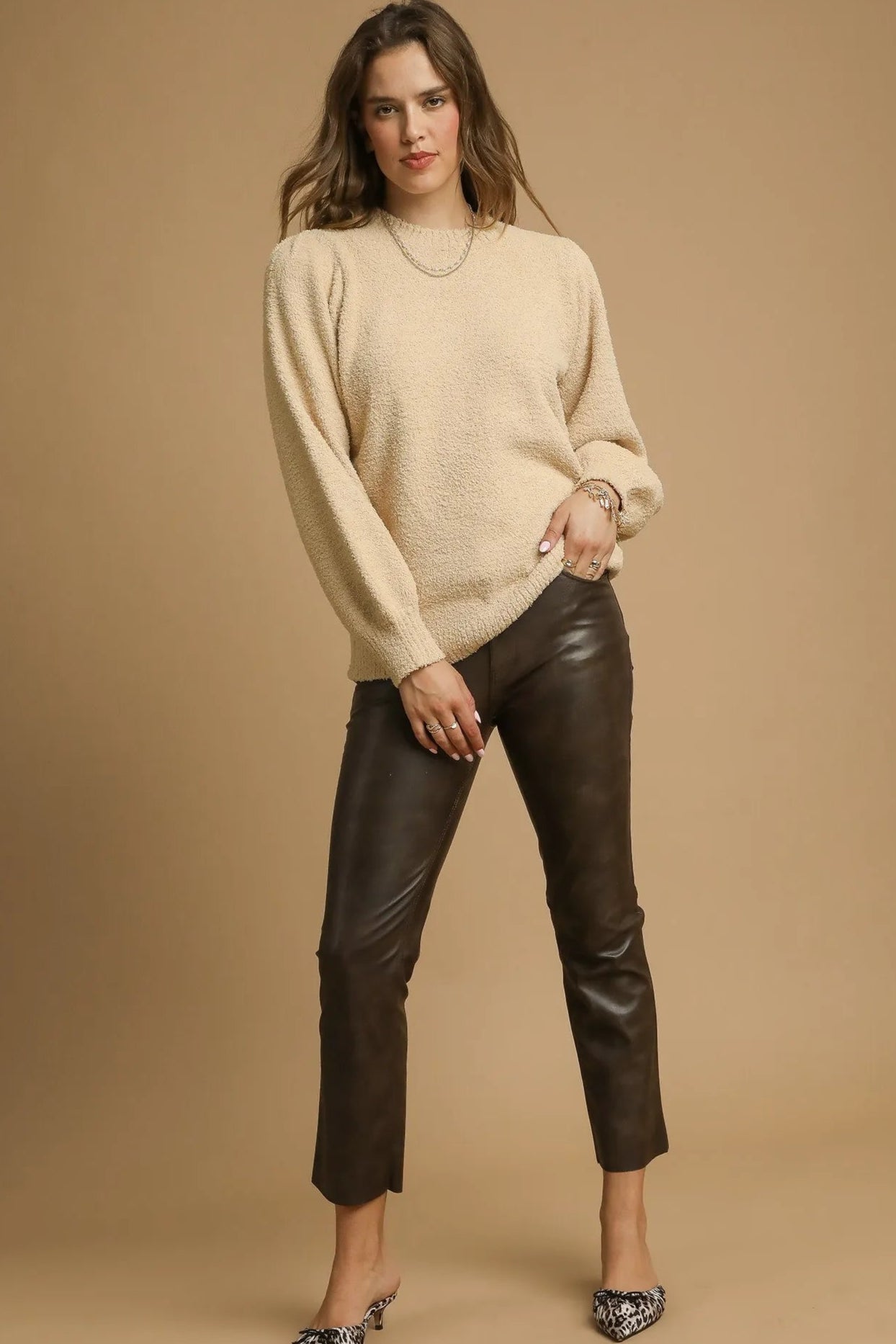 Woman wearing a beige sweater and black leather pants against a brown background
