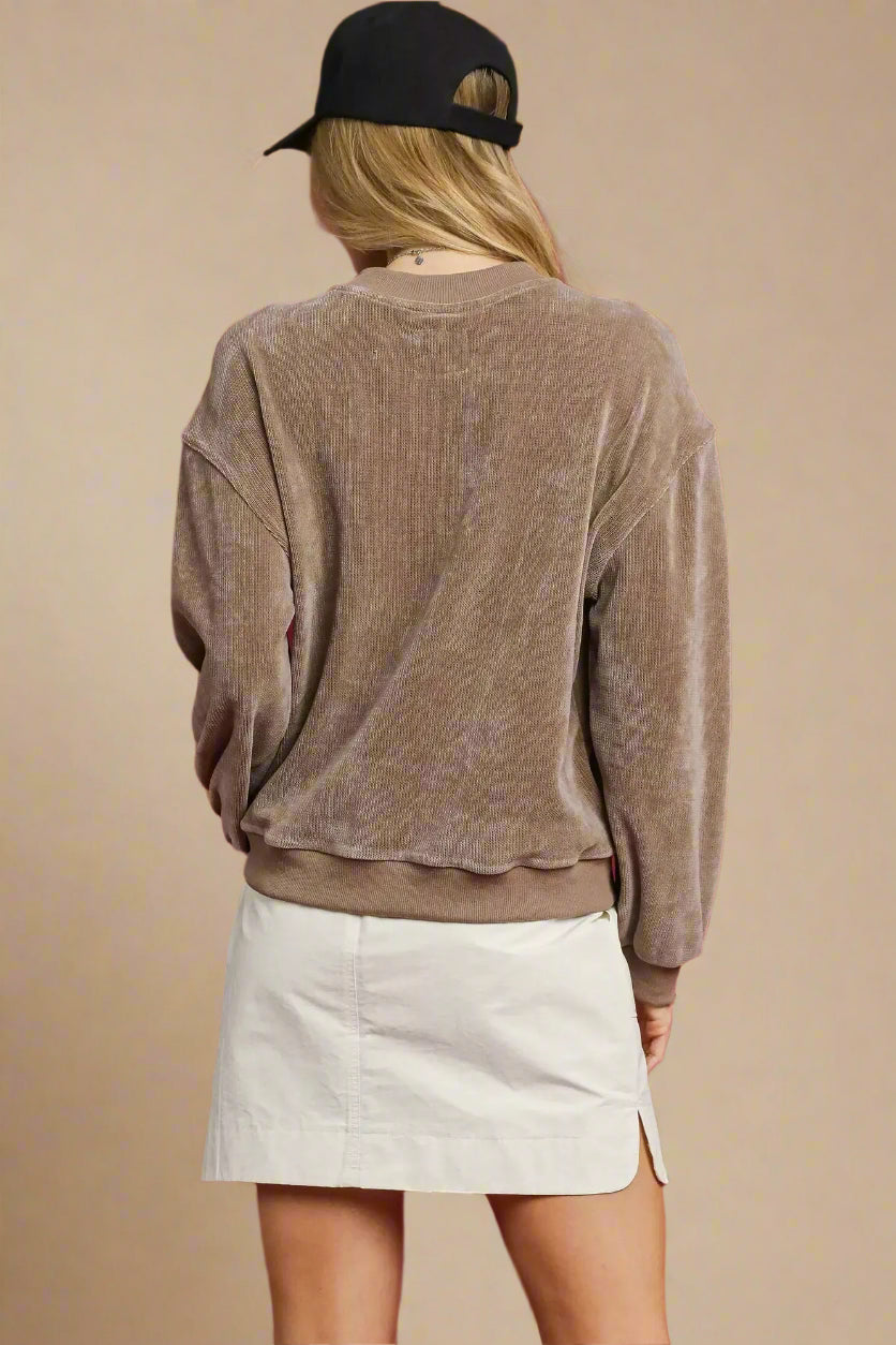 Person wearing a brown velour sweater and white skirt against a red background