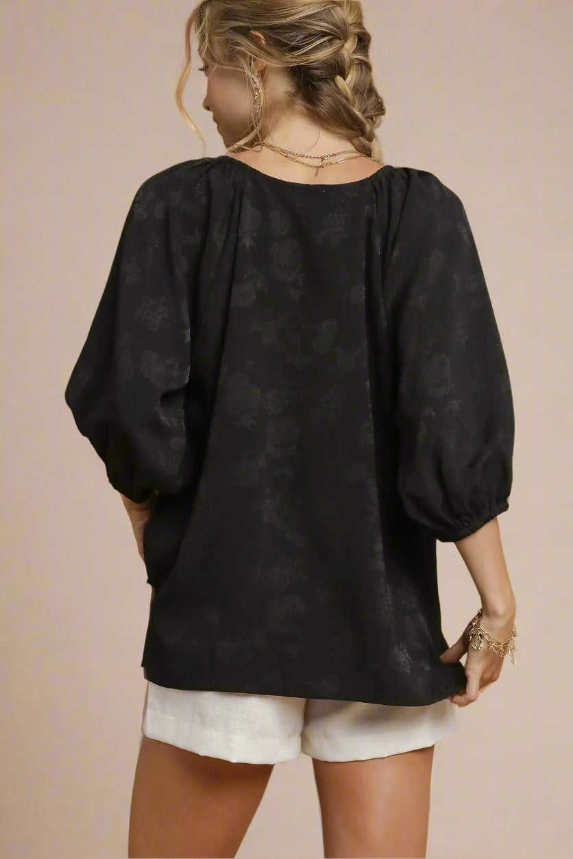 Woman wearing a black blouse with puff sleeves on a beige background